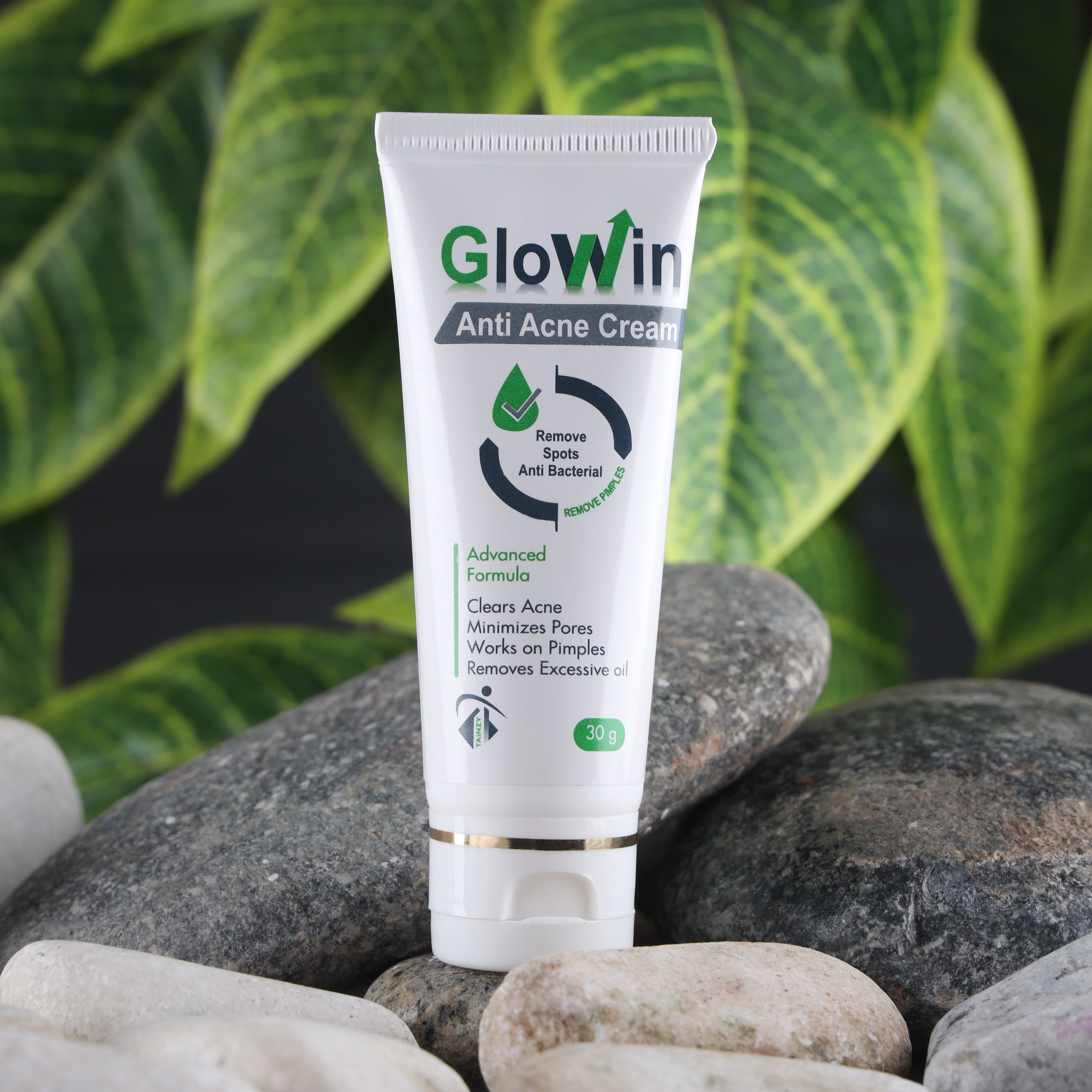 Tube of anti-acne cream for pimples and spots, displayed on stones with green leaves in background.
