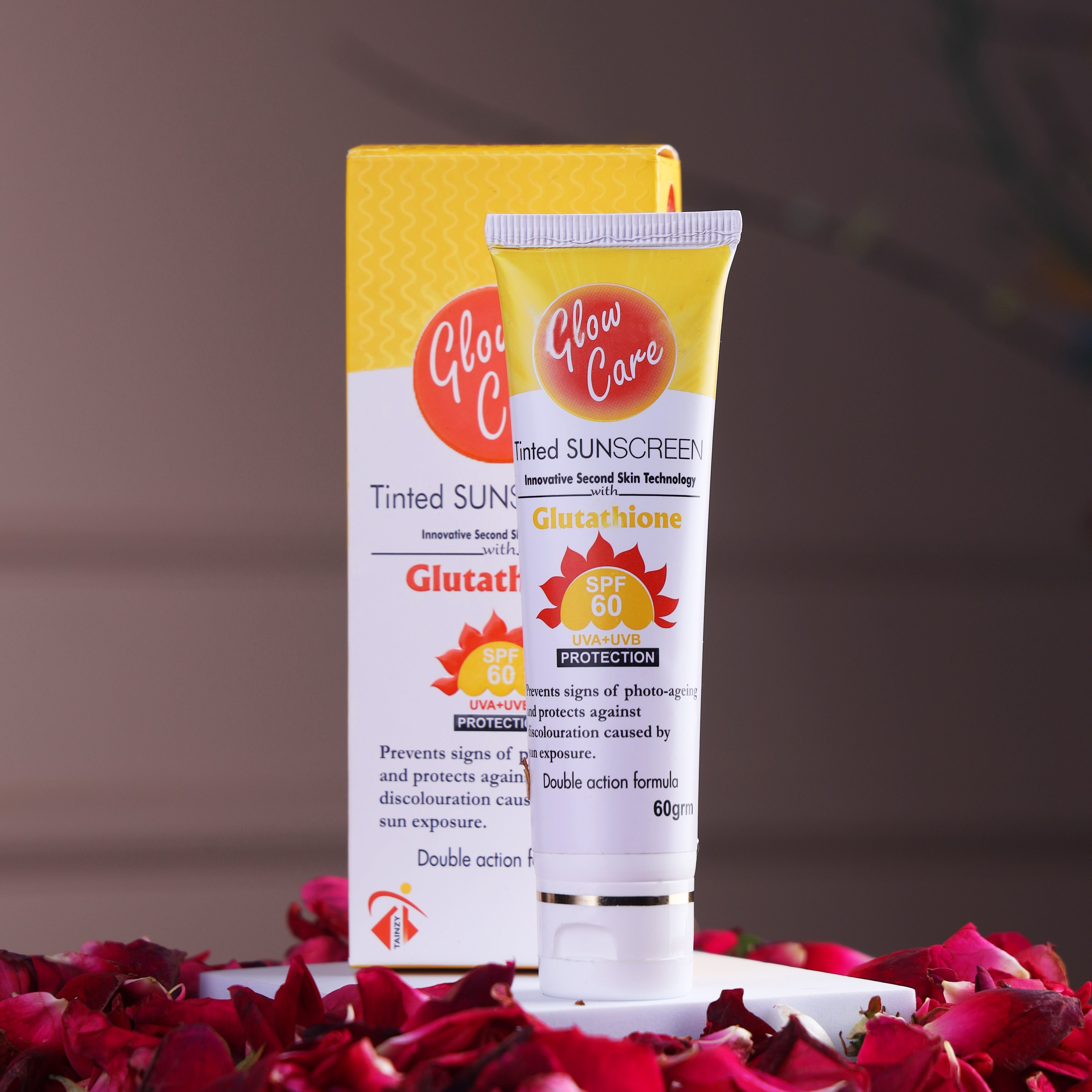 Glow Care tinted sunscreen SPF 60 with glutathione, tube and box on rose petals