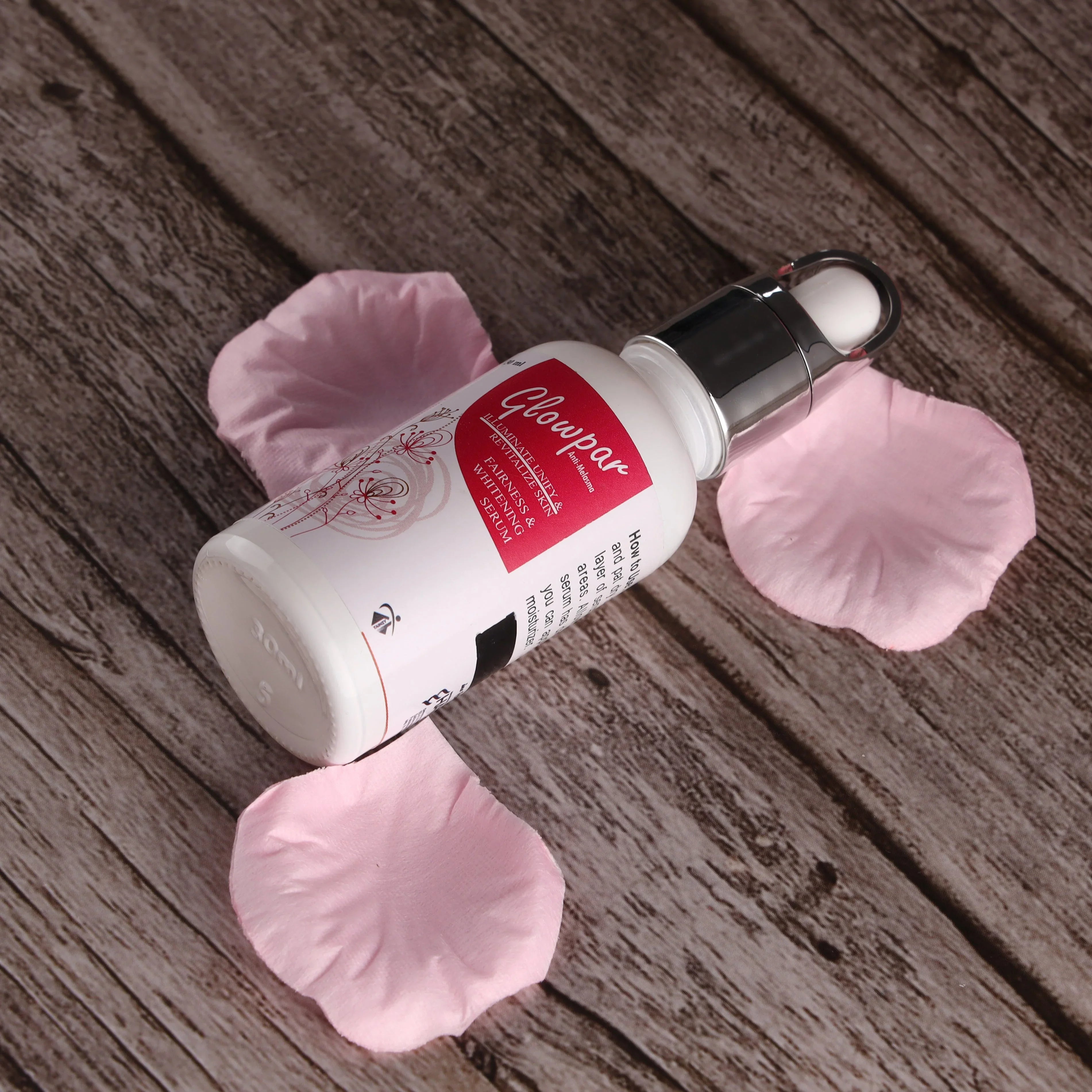 Whitening serum skincare bottle with dropper surrounded by pink rose petals on wooden surface