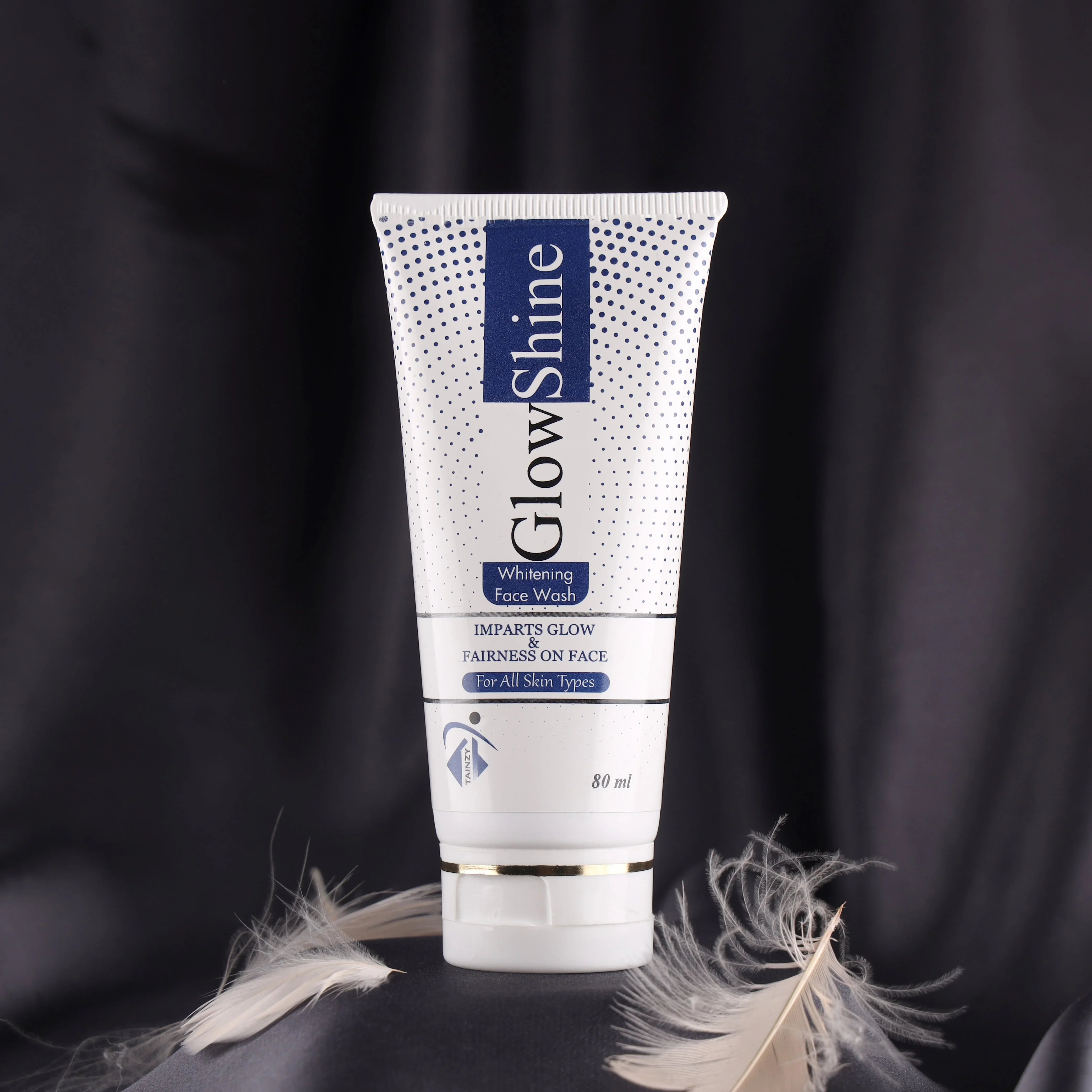 GlowShine whitening face wash tube for all skin types with feathers on a dark background
