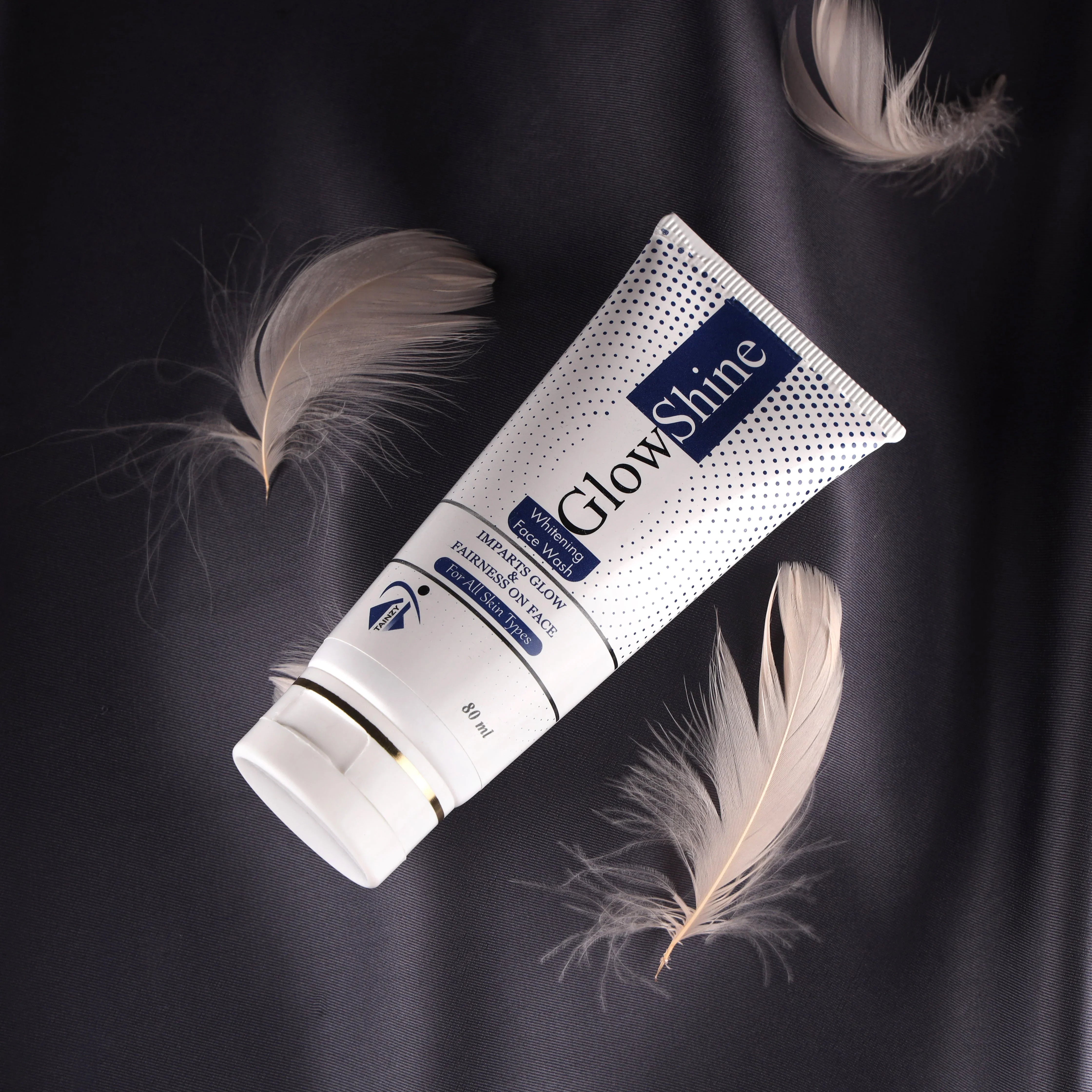 GlowShine whitening face wash tube on dark silk fabric with soft feathers, skincare product