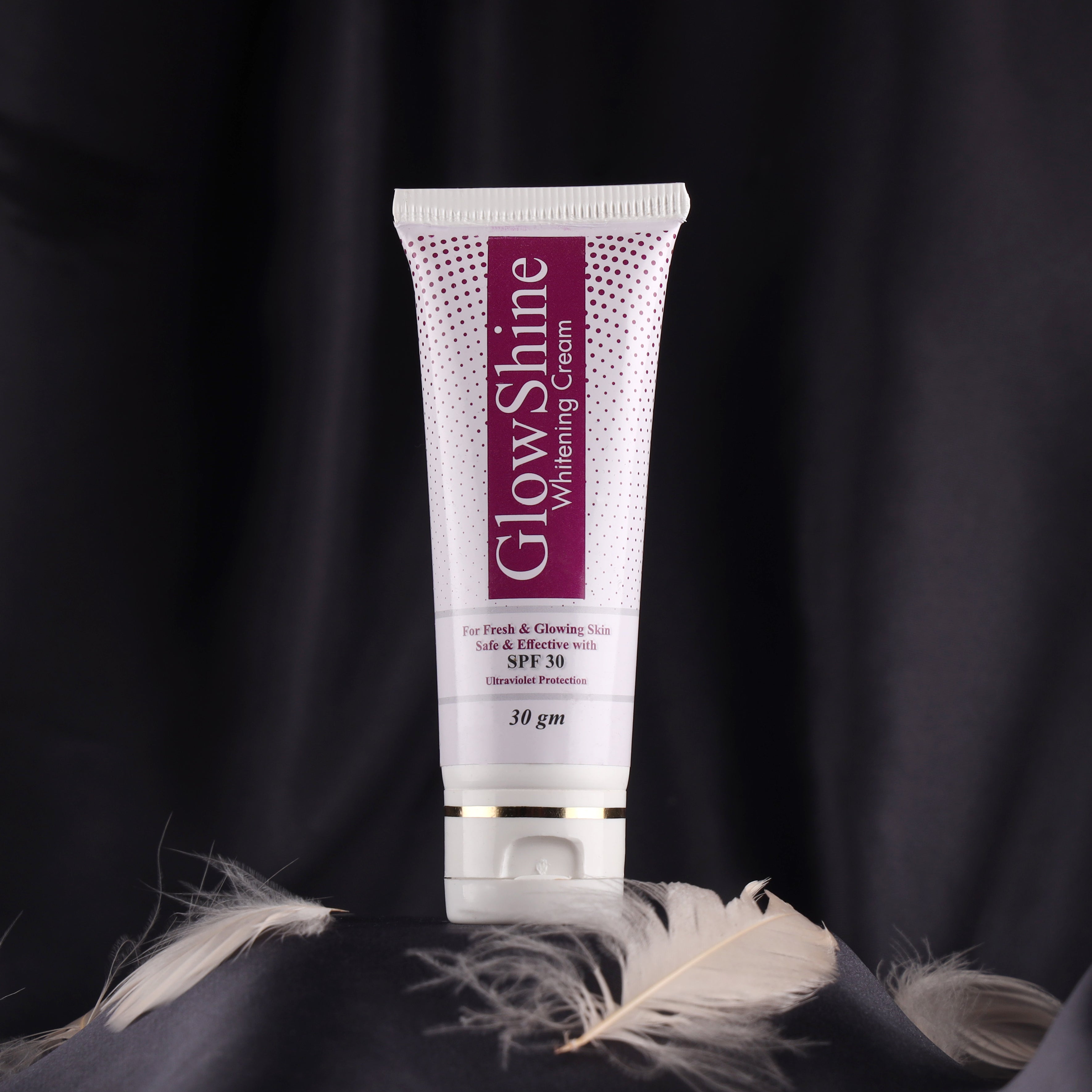 GlowShine whitening cream tube with SPF 30 for glowing skin, on a black satin background with feathers