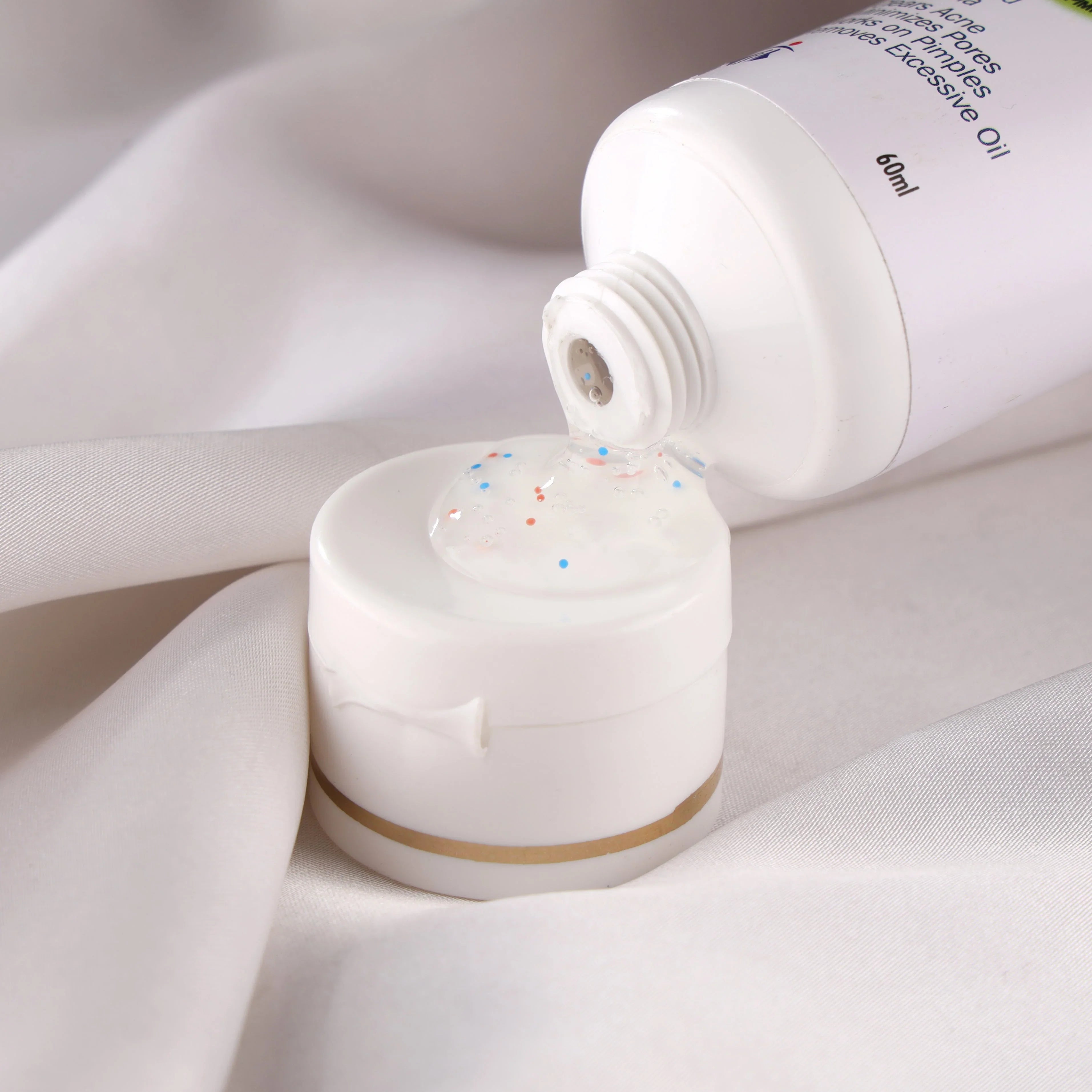 White skincare gel with colorful beads pouring from tube on soft fabric background