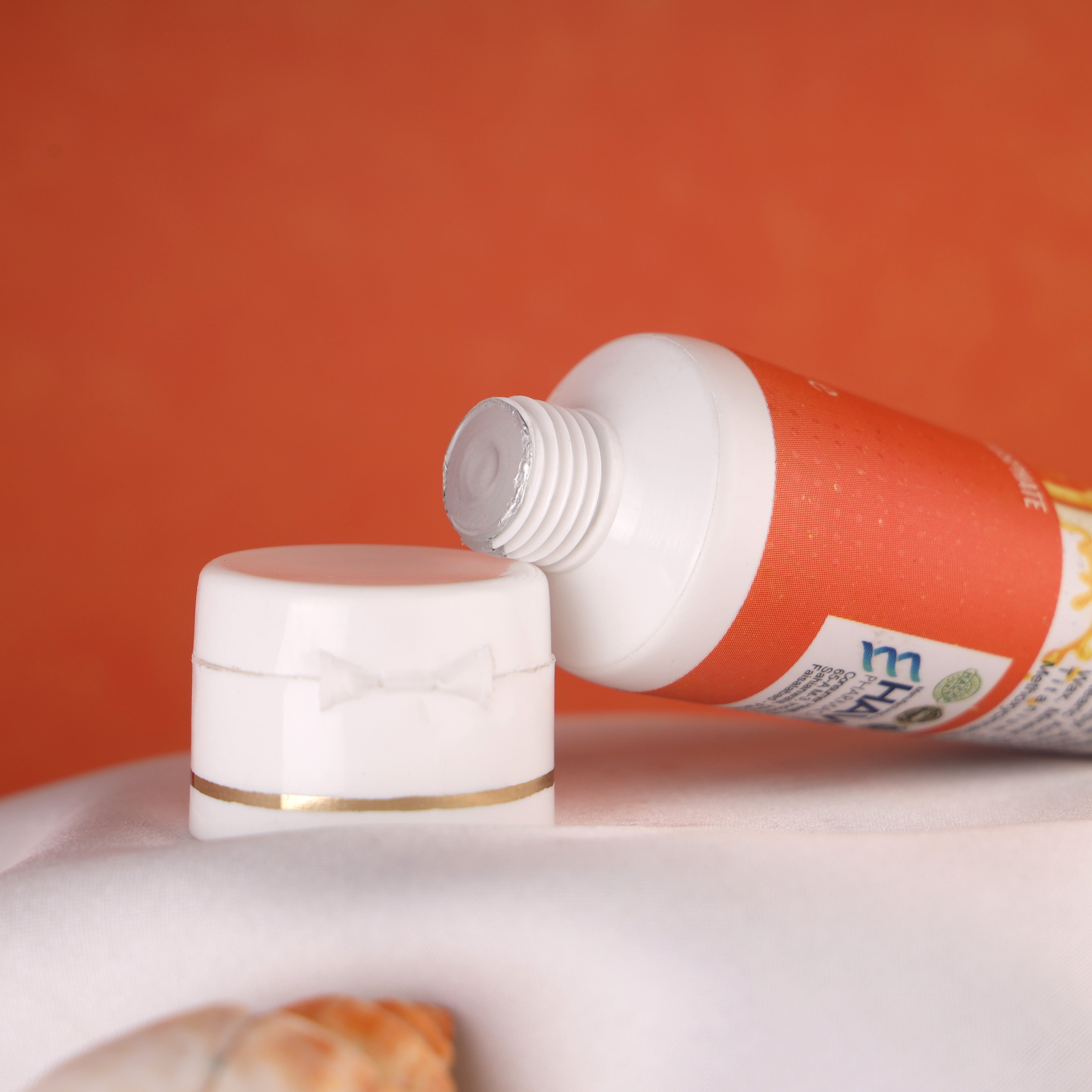 Unopened skincare cream tube with white cap on white fabric, orange background