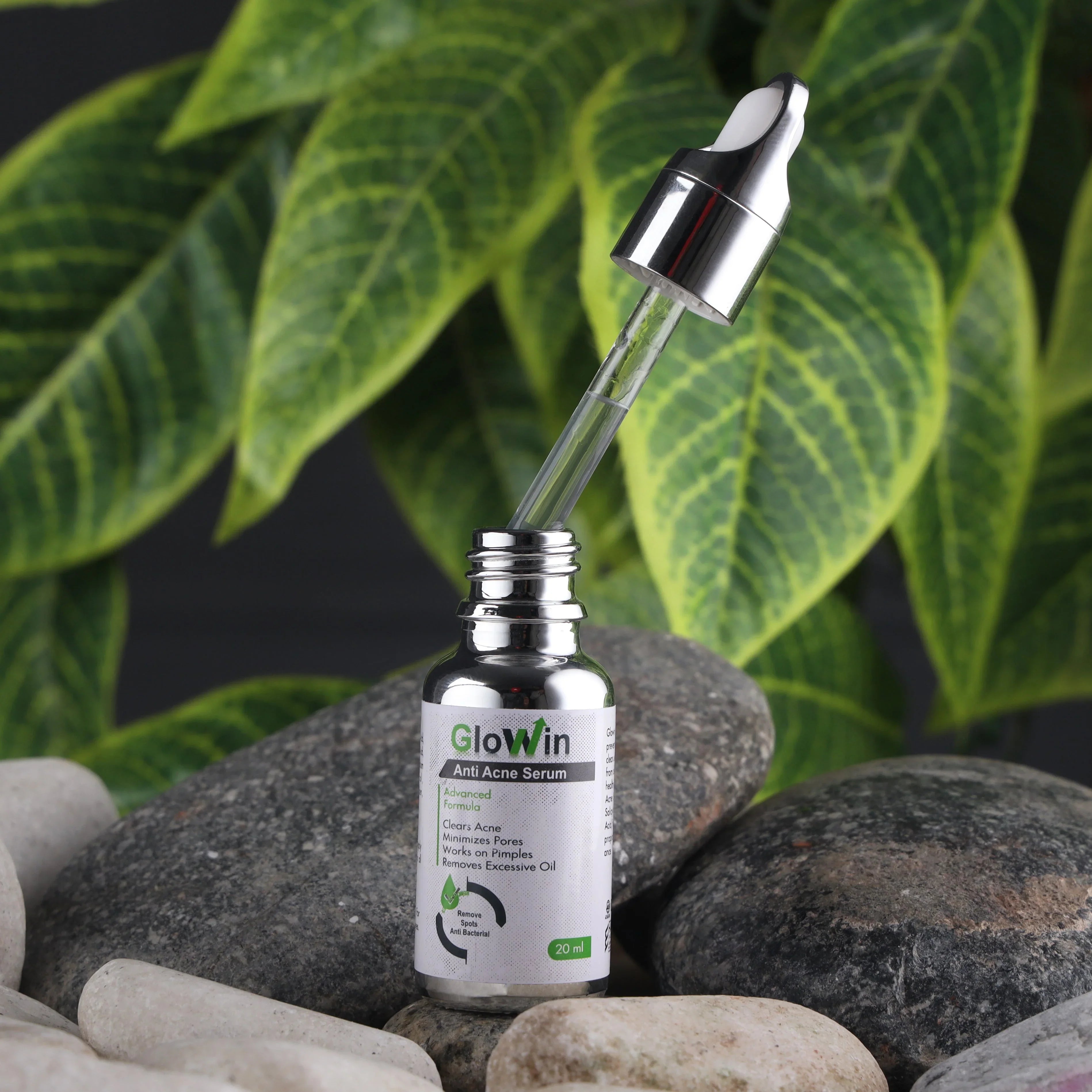 GlowWin anti-acne serum bottle with dropper on rocks, green leaves background, skincare product