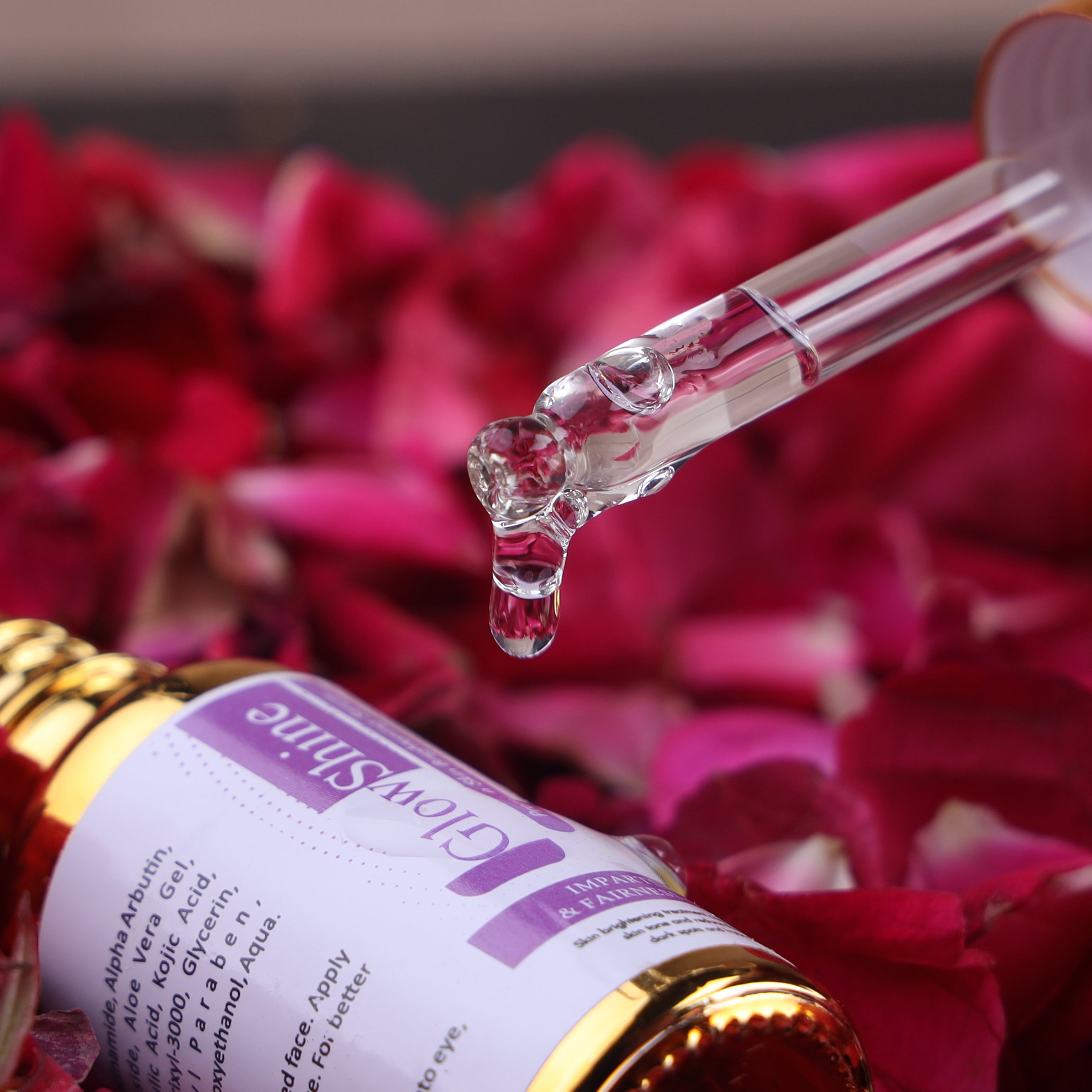 Facial serum dropper with clear liquid above a skincare bottle labeled 'GlowShine' on rose petals