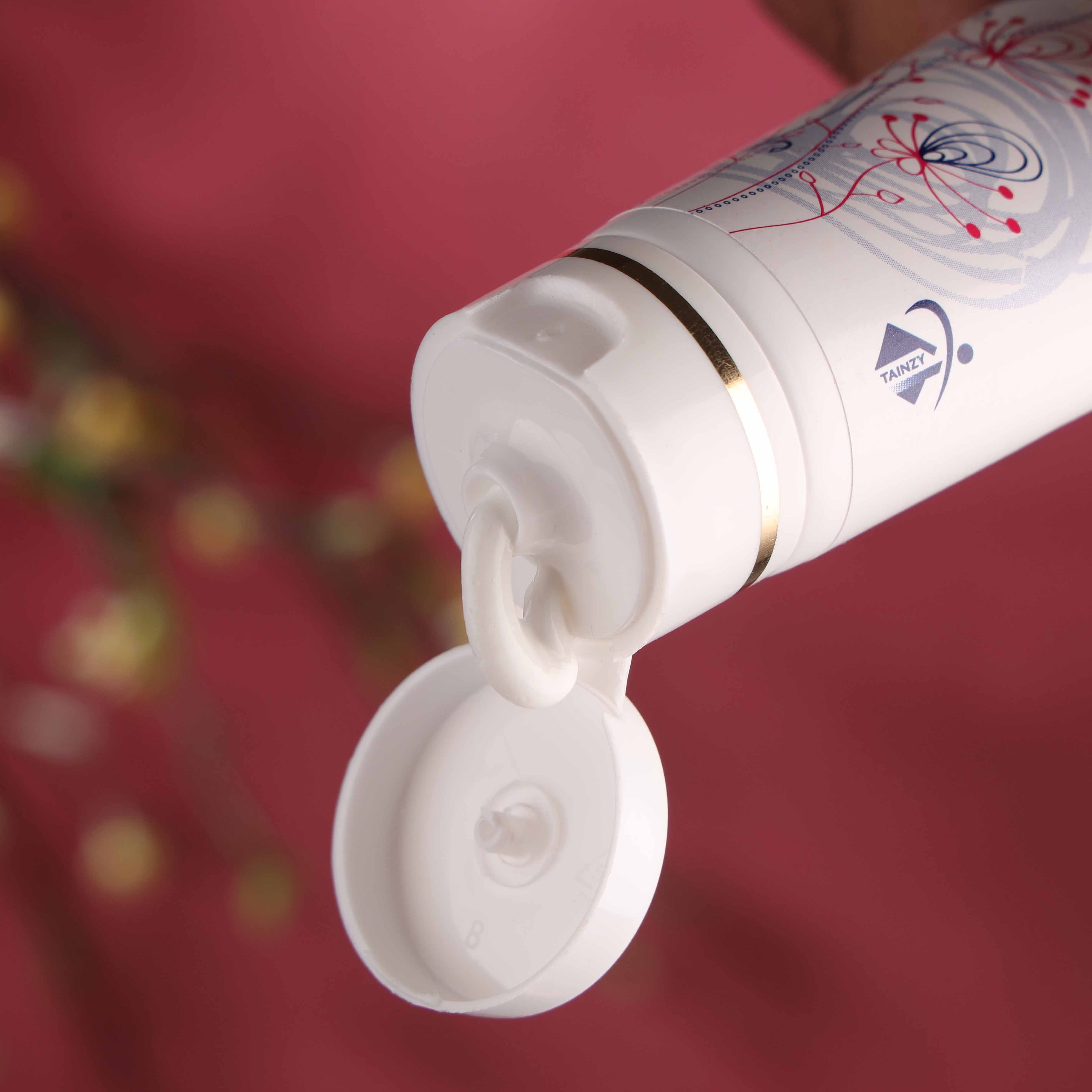 Cream tube with floral design and open flip cap, skincare product on pink background