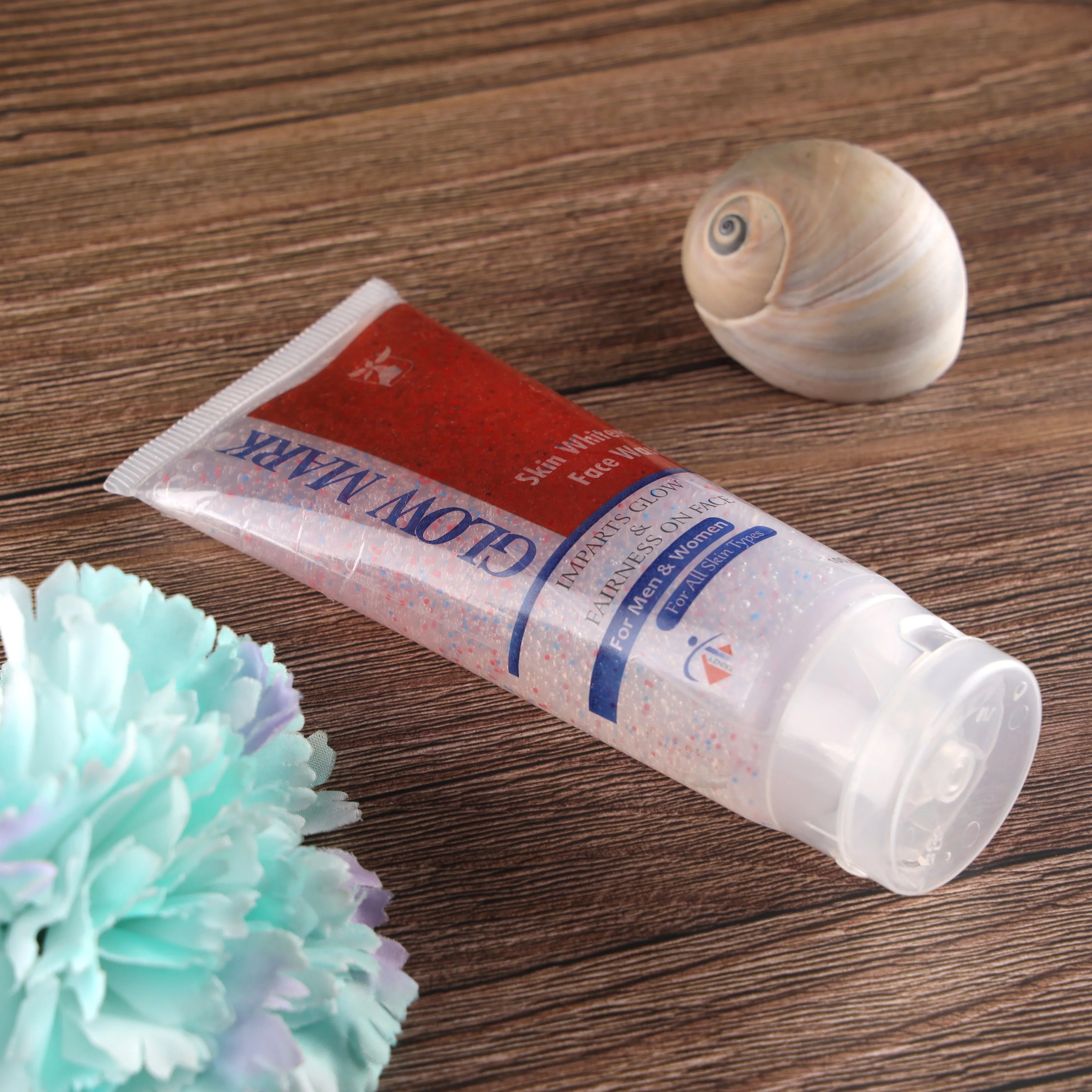 Tube of skin whitening facial scrub with exfoliating beads, flower and shell on wooden surface