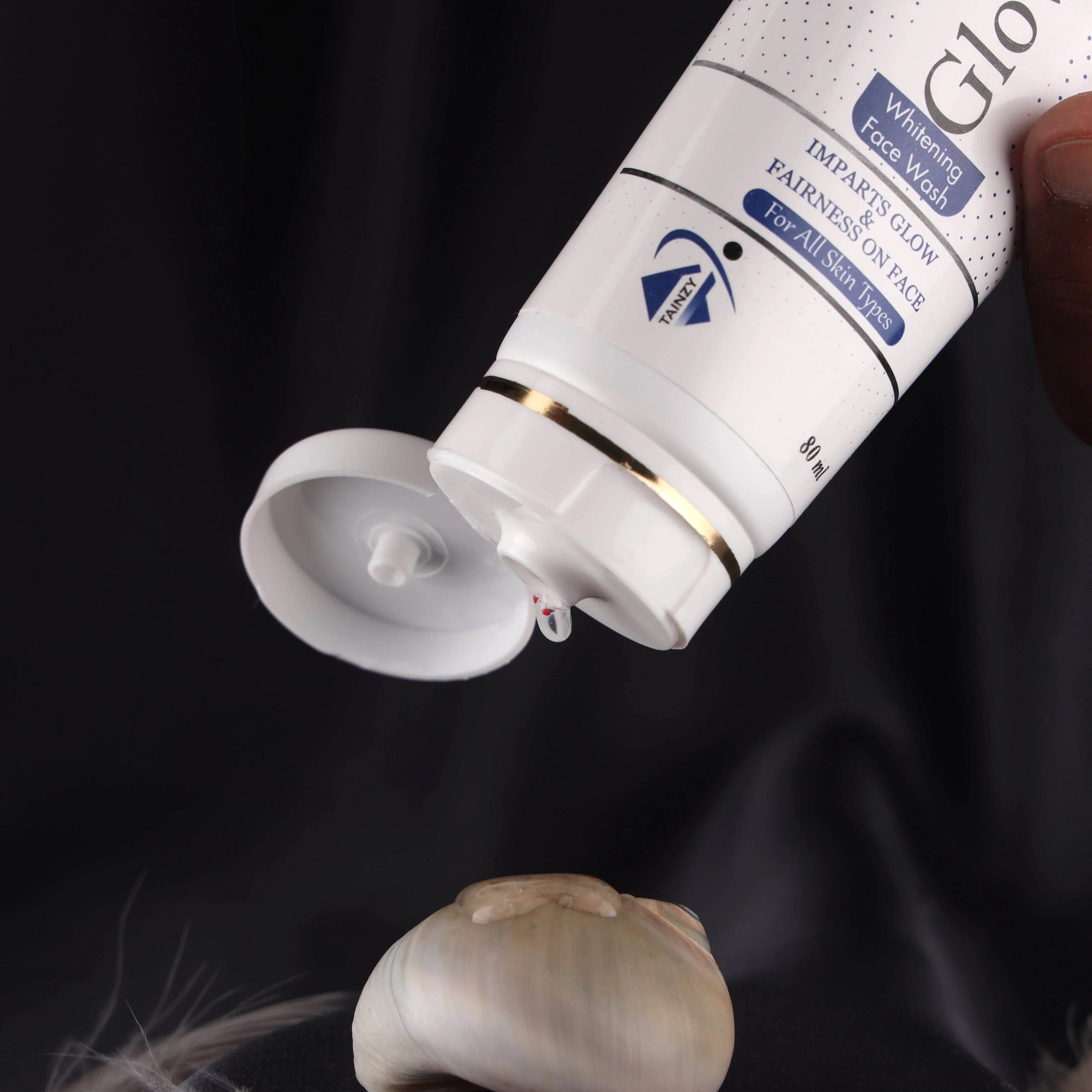 Whitening face wash tube for all skin types with product dispensed on a seashell, black background