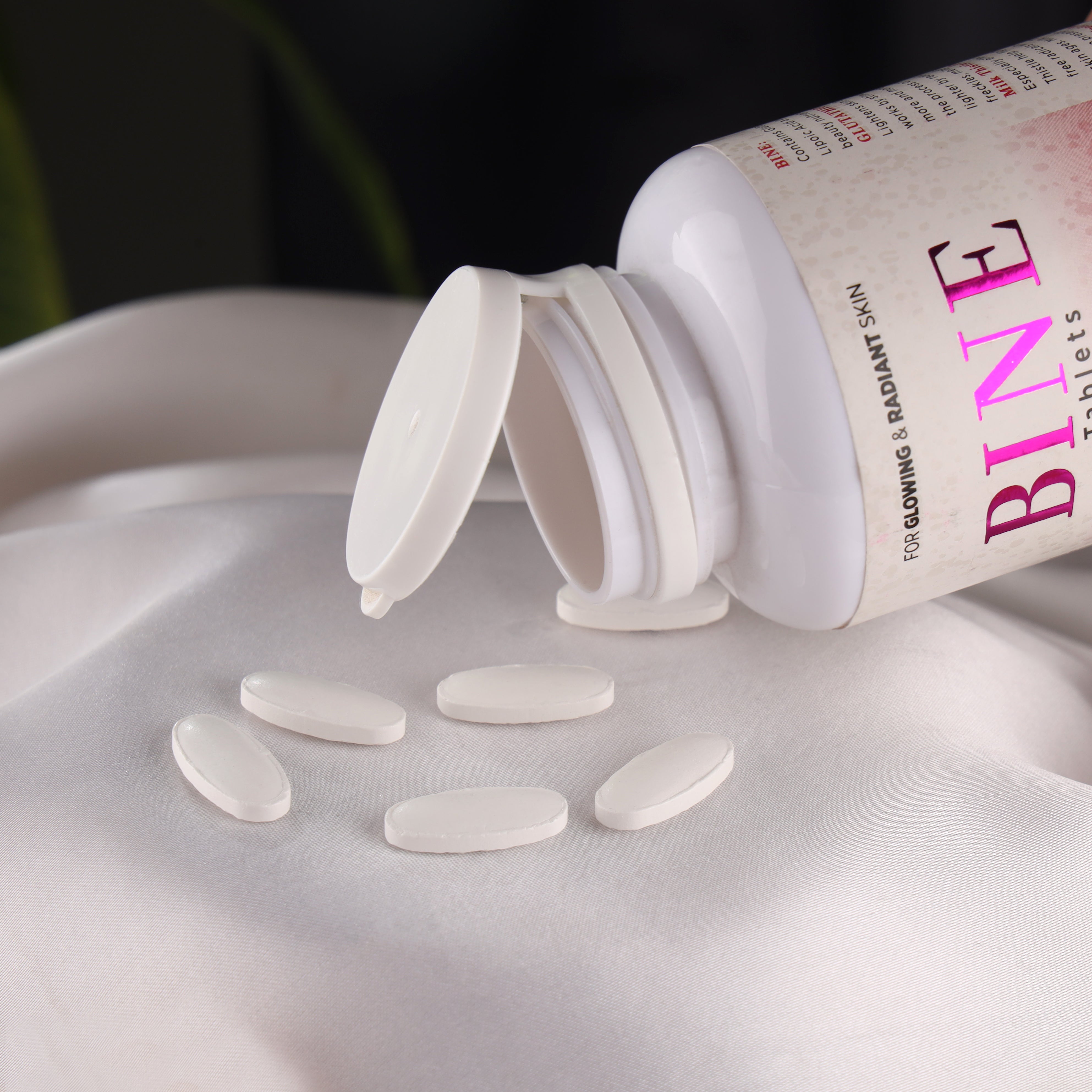 White skincare supplement tablets spilling from bottle labeled for glowing radiant skin