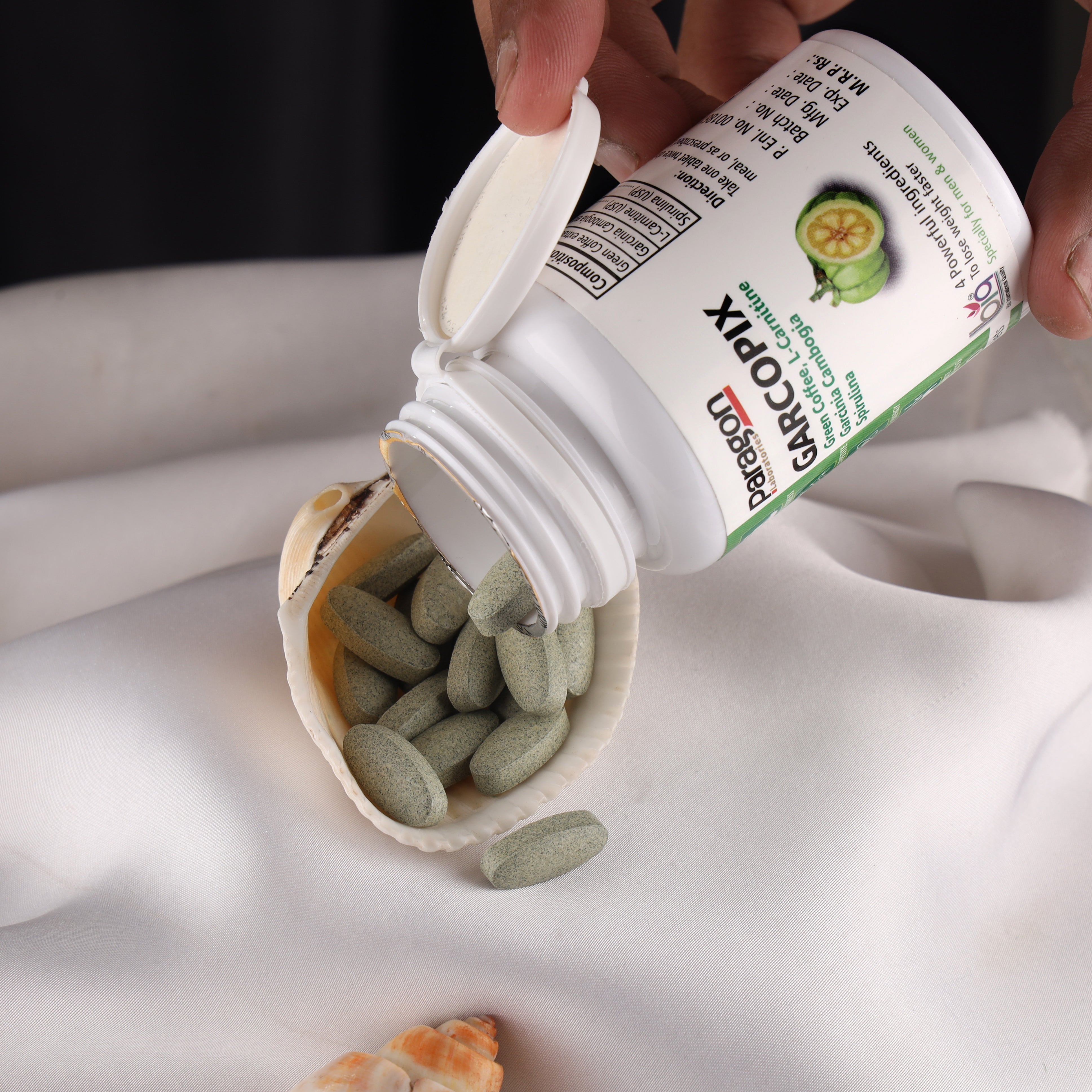 Garcopix dietary supplement tablets spilling from bottle onto white cloth, close-up
