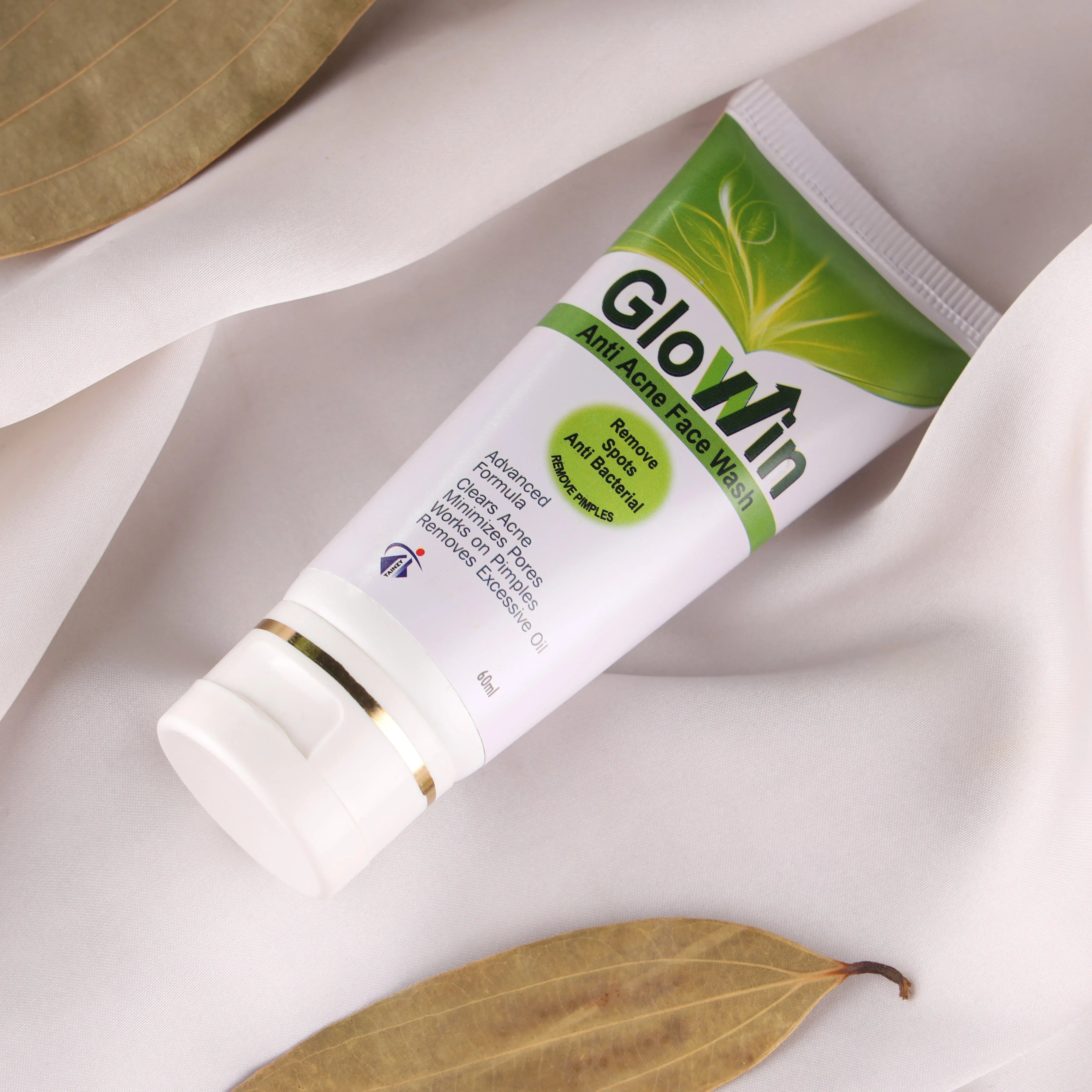 Glowin anti-acne face wash tube for acne treatment on white fabric with dried leaves